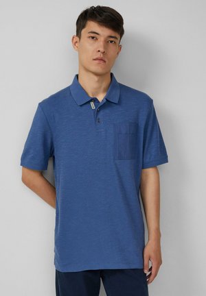 Blauwe poloshirt van een gestructureerde stof, met een knoopsluiting van drie knopen en een opgestikte zak op de linkerkant van de borst. Korte mouwen en een geribbelde kraag.