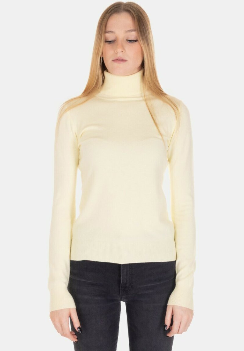 Maglione giallo a collo alto con costine, maniche lunghe, silhouette aderente e texture morbida. Abbinato a jeans scuri per il contrasto.