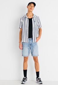 Kreklu ar īsām piedurknēm svītrām baltā un pelēkā krāsā, melnu topu, zilus džinsa šortus, melnas zeķes un sporta apavus ar daudzkrāsainiem akcentiem.