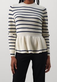 Pull en tricot avec des rayures horizontales marine sur fond crème, une texture côtelée, un ourlet à volant et des manches longues.