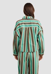 Striped shirt in green, brown, and cream, featuring a classic collar, loose fit, buttoned cuffs, and a pleated back design.
