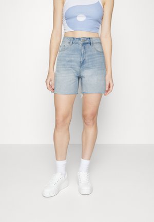 Shorts de mezclilla azul claro con cintura alta, dobladillo deshilachado y bolsillos laterales, combinados con una camiseta corta blanca y zapatillas blancas.