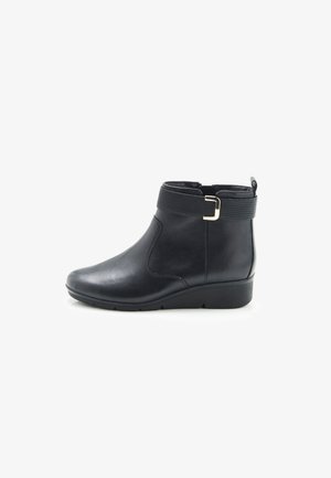 Bottine noire en cuir lisse avec une sangle texturée et un accent de boucle dorée. Dotée d'un bout arrondi et d'un petit talon épais.