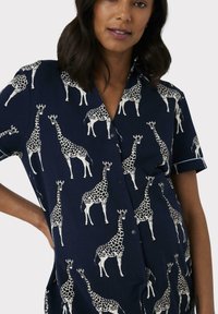 Camisa azul marino con estampado de jirafas en blanco. Mangas cortas con cuello y tapeta de botones. Tela ligera con una textura suave.