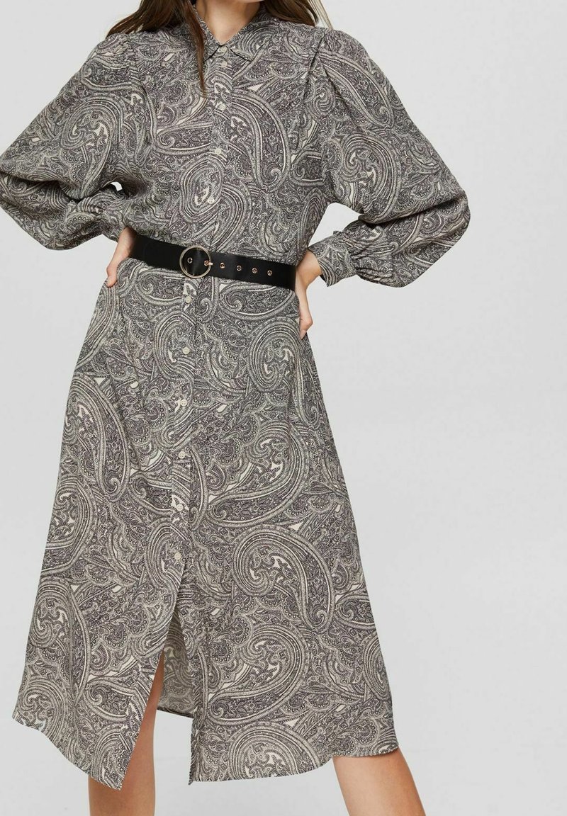 Robe à manches longues avec motif paisley en gris et beige. Elle possède un devant à boutons, une ceinture noire ajustée et un ourlet à hauteur du genou avec une fente à l'avant.
