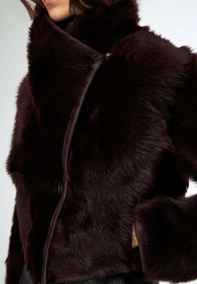 Giacca in pelliccia sintetica color bordeaux con ampio colletto, dotata di rifinitura in pelle liscia e chiusura con bottoni nascosti, caratterizzata da una texture morbida in tutta la superficie.