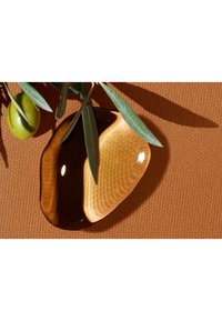 Plat en céramique marron au fini brillant, de forme irrégulière, avec un motif de grain de bois clair. Entouré d'olives vertes et de feuilles d'olivier sur une surface orange texturée.