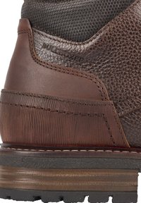 Botas de cuero marrón con acentos texturizados, costuras detalladas y una suela de goma robusta. Presenta una sección superior suave y un tacón ligeramente elevado.