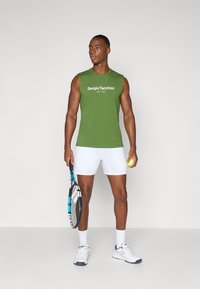 Grøn ærmeløs skjorte med hvid tekst "Sergio Tacchini EST. 1966". Bæres med hvide shorts og holder en tennisketsjer og bold.