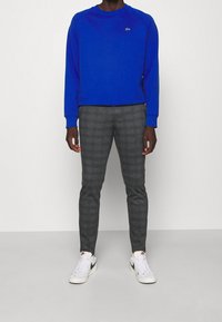 Blauwe sweatshirt met ronde hals, geribbelde manchetten, gecombineerd met grijze geruite broek, gedragen met witte Nike-sneakers met zwarte accenten.