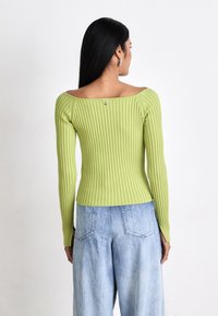 Maglione verde a coste con scollatura ampia e maniche lunghe, abbinato a jeans in denim azzurro chiaro e comodi. Accentuato da un piccolo dettaglio sul retro.