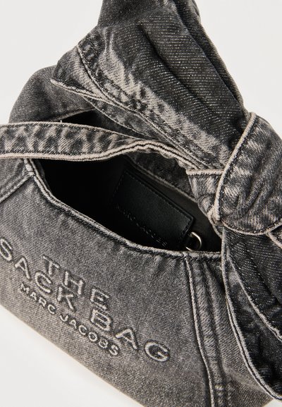 Γκρι τζιν τσάντα Marc Jacobs με κεντημένο το όνομα της μάρκας και λαβή με στριμμένο κόμπο, εμφανιζόμενη μερικώς ανοιχτή.