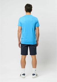 Blå kortærmet skjorte, marineblå shorts, hvide ankelstrømper og sneakers. Glat stoftekstur, afslappet pasform. Minimalistisk design.
