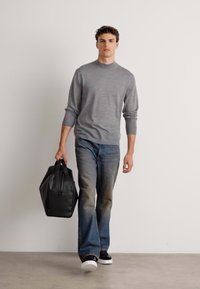 Pelēks džemperis ar apaļu kaklu, tumši zili džinsi un melna ādas soma. Modelis valkā melnus sporta apavus ar baltām zolēm. Minimalistisks dizains, ikdienišķs izskats.