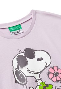 Fialová košile se Snoopym v slunečních brýlích, který drží růžový květ, s etiketami United Colors of Benetton a Peanuts.