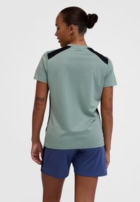 Activewear shirt in light green with black shoulder accents. Short sleeves, smooth texture, paired with navy shorts. Simple design.