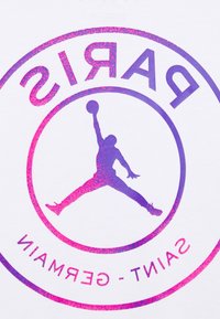 Vit t-shirt med en stor cirkulär grafik som har "PARIS" i lila och rosa, samt en silhuett av en basketspelare i en hoppande pose.