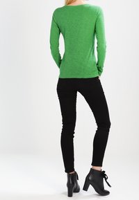 Camicia verde a maniche lunghe in tessuto morbido, abbinata a jeans skinny neri e stivaletti neri con dettagli in pizzo.
