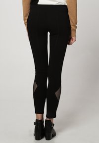 Leggings neri con pannelli in rete, design aderente e dettagli cuciti. Il materiale sembra elastico e liscio, adatto per l'abbigliamento sportivo.
