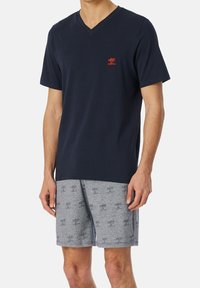 Camiseta de cuello en V de color navy con un pequeño logo rojo en el pecho, combinada con pantalones cortos grises con un patrón de palmeras. Tejido de mezcla de algodón, corte relajado.