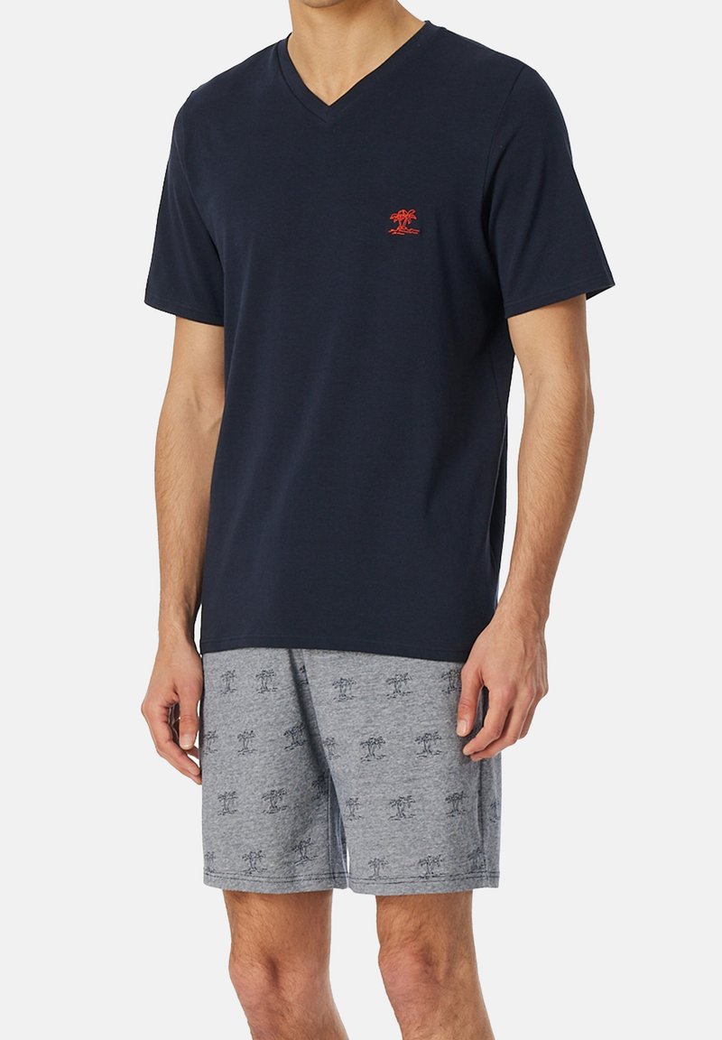 Camiseta de cuello en V de color navy con un pequeño logo rojo en el pecho, combinada con pantalones cortos grises con un patrón de palmeras. Tejido de mezcla de algodón, corte relajado.