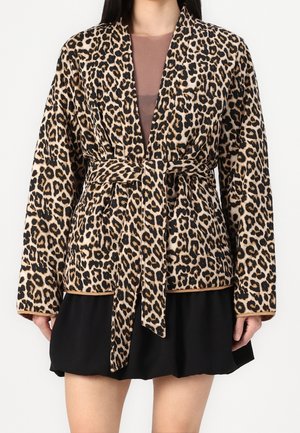 Vestaglia con stampa leopardata in tessuto morbido, con maniche lunghe, cintura in vita e dettagli contrastanti color beige. Indossata sopra un top aderente e una gonna nera.