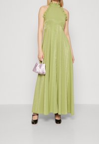 Maxi dress in light green, featuring a ruffled halter neck, shiny texture, and flowing silhouette. Paired with a small lavender purse and black shoes.