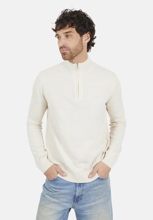 Beige kwart-rits pullover trui van zachte stof, met lange mouwen en een geribde kraag, gedragen met blauwe jeans.