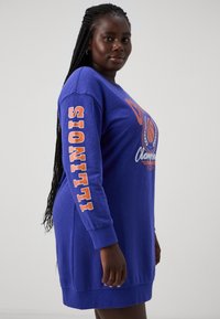 Μπλε φόρεμα με μακριά μανίκια που διαθέτει την ένδειξη "ILLINOIS" σε πορτοκαλί στο μανίκι, αθλητικό σχέδιο και στρογγυλή λαιμόκοψη. Μαλακή υφή και άνετη εφαρμογή.