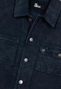 Marinblå kord skjorta med metallknappar, två framfickor och en klassisk krage. Strukturerad tyg med vertikal ribbning. Märke inuti.