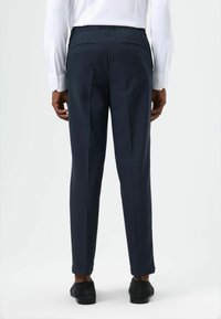 Dunkelblaue Hose mit geradem Schnitt, elastischem Bund und zwei Gesäßtaschen. Getragen mit einem weißen Hemd und dunklen Schuhen.