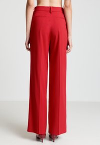 Rote, weit geschnittene Hosen mit maßgeschneiderter Passform, mit einer glatten Textur und zwei Gesäßtaschen. Der Saum endet oberhalb des Knöchels.