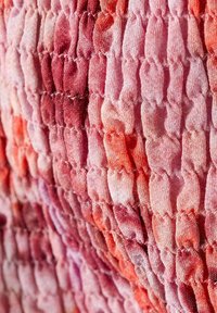 Detail růžového a červeného texturovaného materiálu se sbíraným, elastickým, vroubkovaným vzorem vytvářejícím svislé hřebeny.