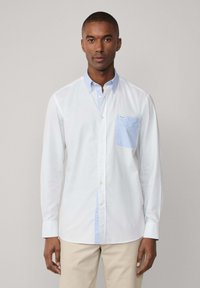 Camicia bianca a maniche lunghe con colletto button-down azzurro e tasca. Caratterizzata da un delicato motivo testurizzato e dettagli blu sui lati.