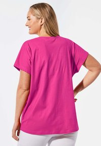 Kurzarm, lockeres T-Shirt aus leuchtend pinkem Baumwollstoff, mit einem runden Halsausschnitt und einem längeren Rücken. Keine sichtbaren Muster oder Hardware.