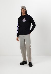 Sort langærmet T-shirt med grafisk tryk på brystet og lilla bogstaver på ærmet, parret med lyse denimjeans og sorte chunky støvler.