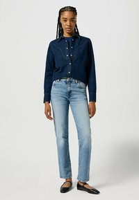 Mörk denimskjorta med västerninspirerad söm och pärlfärgade tryckknappar, i kombination med ljusblå raka jeans och svarta platta skor.