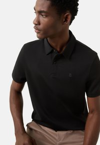 Czarna koszulka polo z subtelnym logo na piersi, krótkimi rękawami i klasycznym kołnierzykiem, wykonana z gładkiego, lekkiego materiału.