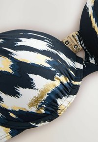Top bikini imbottito blu navy e bianco con dettagli dorati, caratterizzato da un motivo astratto e una chiusura a gancio in metallo. Tessuto morbido.