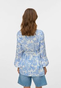 Blusa blu chiaro con maniche lunghe, caratterizzata da un motivo a foglia, vita cintrata e polsini arricciati. Abbinata a pantaloni shorts di denim.