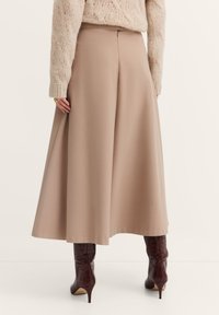 Beige Culottes aus weichem Stoff mit ausgestellter Silhouette, ausgestattet mit einem Reißverschluss hinten und einer glatten Verarbeitung. Getragen mit kniehohen braunen Stiefeln.