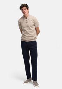 Beige kortermet polo-skjorte med krage og tre knapper, sammen med marineblå rettskåret bukser og grå sko.