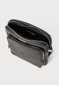 Schwarze Kunstledertasche mit geprägtem Muster, doppelten Reißverschlussfächern, silberner Hardware und Innenfutter aus Stoff mit Logoprint.