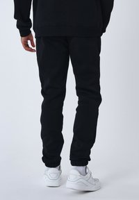 Joggers negros con cintura elástica y tobillos ajustados. Combinados con zapatillas blancas, que presentan una textura suave y un diseño ajustado.