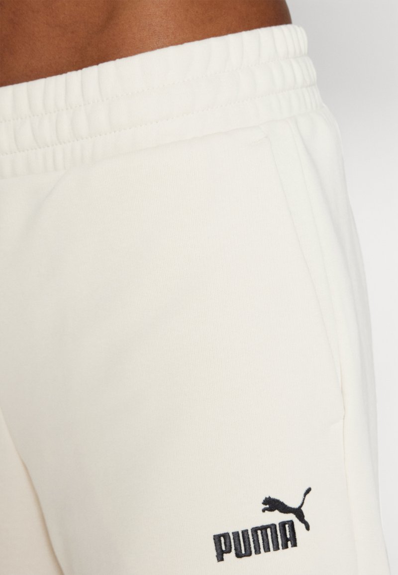 Helle Creme Sweatpants mit elastischem Bund, ausgestattet mit Seitentaschen und einem schwarzen, gestickten Puma-Logo in der Nähe der linken Tasche.