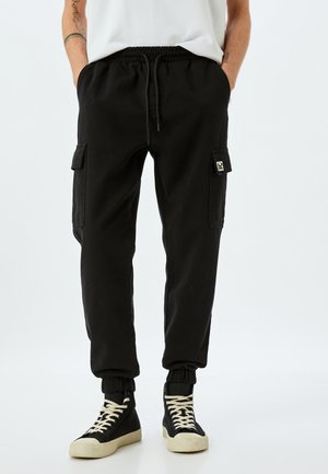 Zwarte cargobroek met een elastische tailleband, verstelbaar trekkoord en zijzakken; beschikt over elastische boorden en een klein logopatch.
