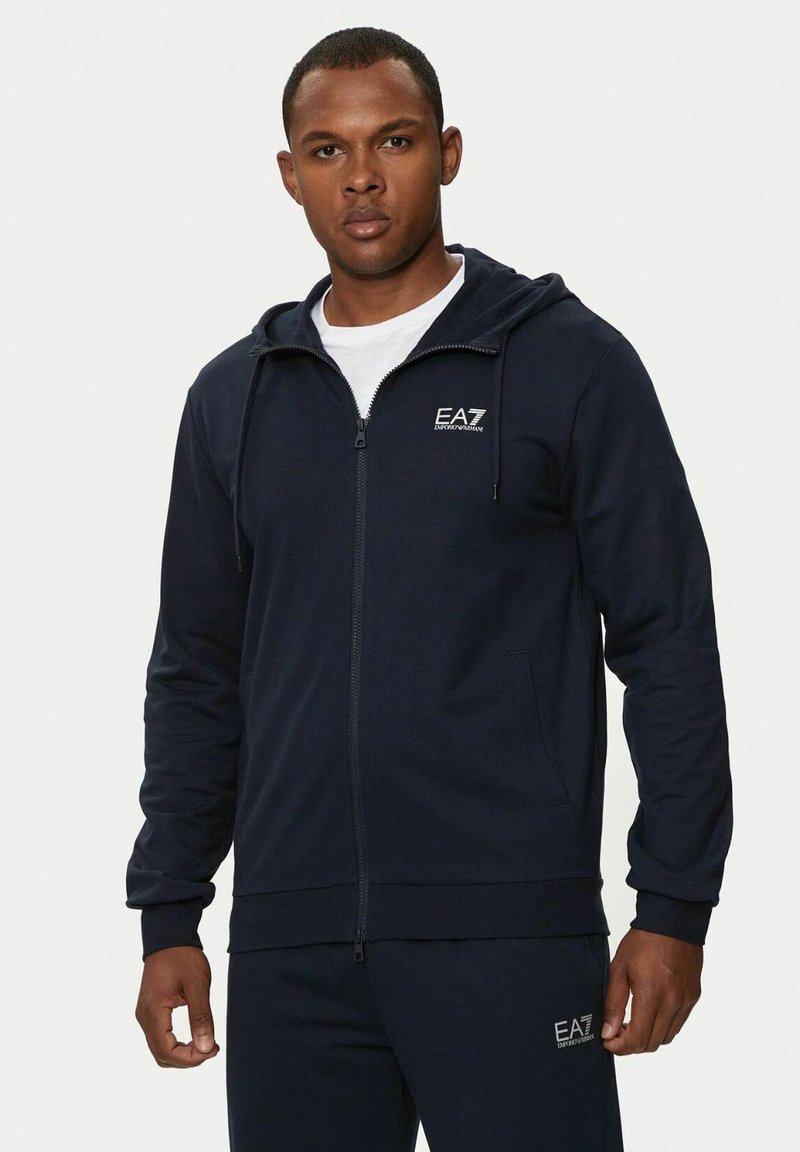 Felpa con zip navy realizzata in tessuto morbido, con cappuccio regolabile e logo sul petto. Include tasche laterali e polsini a coste.