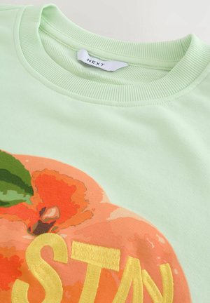 Sweatshirt en coton vert menthe avec un grand motif de pêches et des accents orange, vert et jaune, ainsi qu'un col rond côtelé.