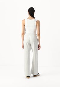 Gray sweatpants with a relaxed fit and elastic waistband, paired with a white tank top. Black and white sandals complete the outfit.