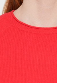 Red rib-knit sweater with a round neckline, featuring a soft texture and subtle stretch. Visible seams along the collar.